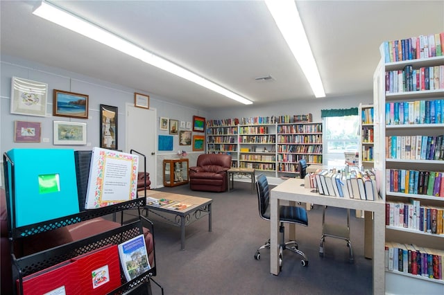 carpeted office space featuring visible vents and wall of books