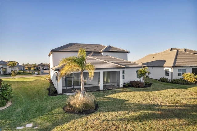 back of property with a tile roof, a yard, and stucco siding