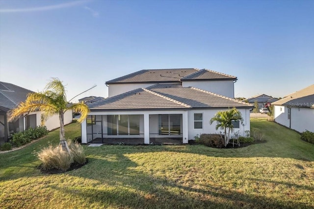 rear view of house with a sunroom, a tile roof, and a lawn