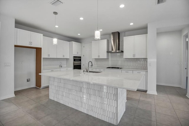 kitchen with visible vents, double oven, white cabinetry, a sink, and wall chimney exhaust hood