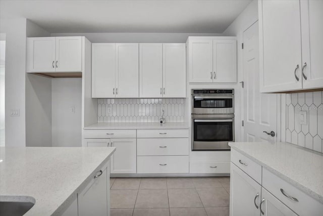 kitchen with double oven, light stone countertops, white cabinets, and tasteful backsplash