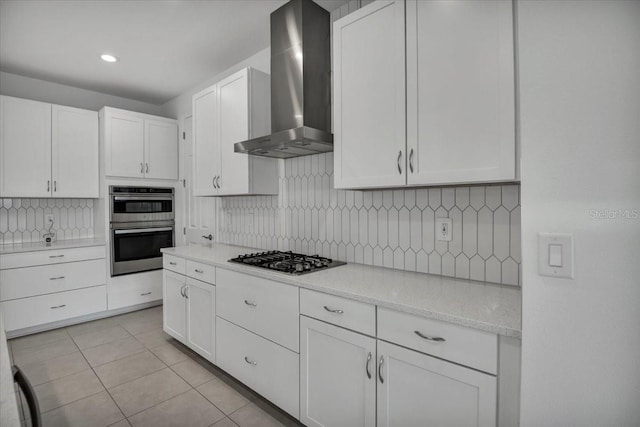 kitchen featuring light tile patterned floors, stainless steel appliances, tasteful backsplash, white cabinetry, and wall chimney range hood