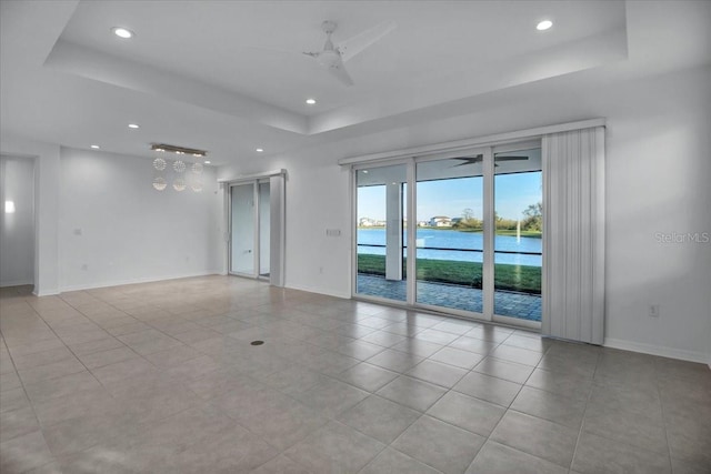 empty room with baseboards, a ceiling fan, a water view, a tray ceiling, and recessed lighting