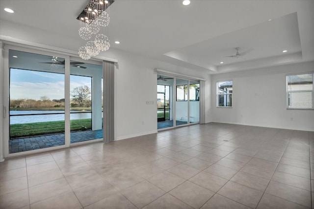 unfurnished room featuring ceiling fan with notable chandelier, a tray ceiling, a water view, and a healthy amount of sunlight