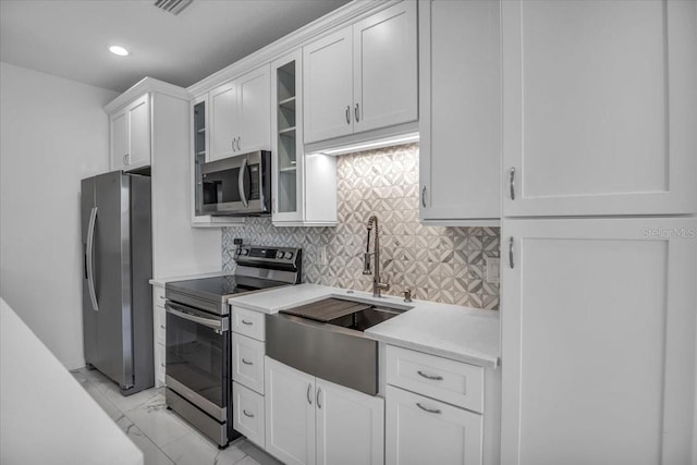 kitchen with a sink, white cabinets, appliances with stainless steel finishes, backsplash, and glass insert cabinets