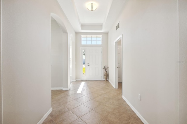 entrance foyer with light tile patterned floors, visible vents, baseboards, arched walkways, and a raised ceiling