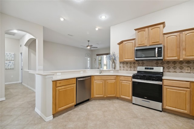 kitchen with stainless steel appliances, light countertops, decorative backsplash, a sink, and a peninsula