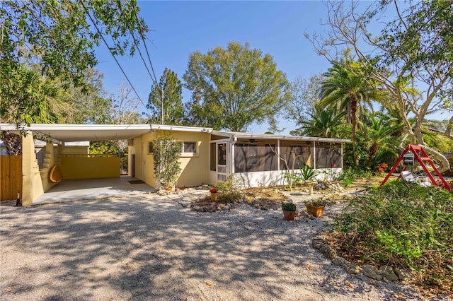 mid-century home featuring a carport, a sunroom, and gravel driveway