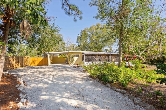 view of front facade with a carport, gravel driveway, fence, and a sunroom