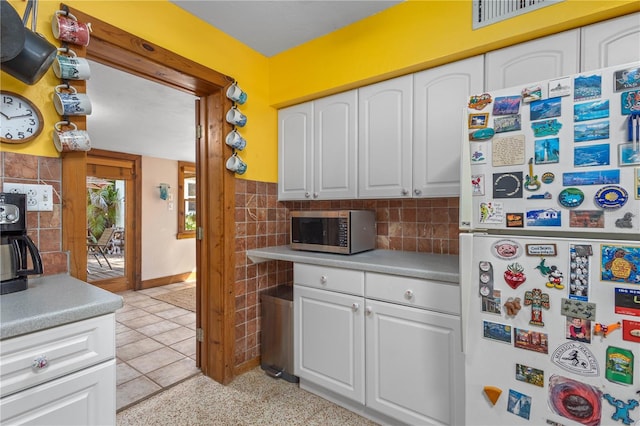 kitchen featuring light countertops, freestanding refrigerator, stainless steel microwave, and white cabinetry