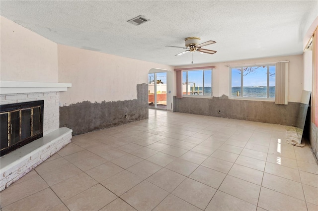 unfurnished living room with visible vents, arched walkways, a ceiling fan, tile patterned floors, and a brick fireplace