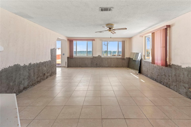 spare room with arched walkways, ceiling fan, a textured ceiling, light tile patterned flooring, and visible vents