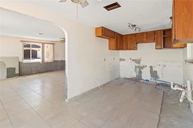 kitchen with arched walkways, a ceiling fan, brown cabinetry, open floor plan, and light tile patterned flooring