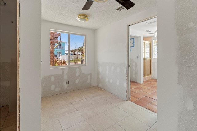 empty room featuring ceiling fan, a textured ceiling, light tile patterned flooring, and a wealth of natural light