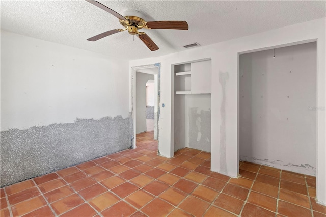 interior space featuring tile patterned flooring, ceiling fan, visible vents, and a textured ceiling