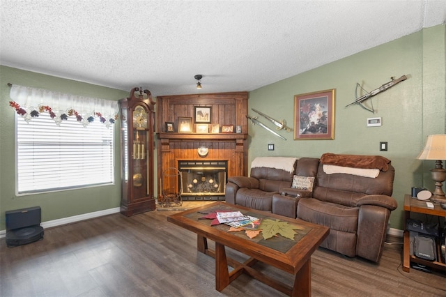 living area featuring a textured ceiling, a fireplace, baseboards, and wood finished floors