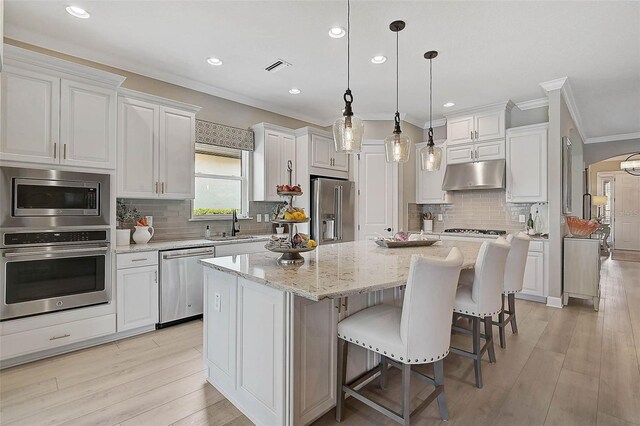 kitchen with white cabinetry, under cabinet range hood, appliances with stainless steel finishes, and a kitchen island