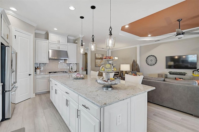 kitchen featuring under cabinet range hood, a kitchen island, ornamental molding, and freestanding refrigerator