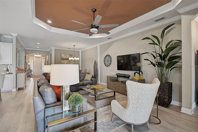 living area with visible vents, ceiling fan with notable chandelier, arched walkways, light wood-style floors, and a raised ceiling