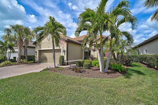 mediterranean / spanish-style home with a tile roof, a front yard, stucco siding, decorative driveway, and a garage