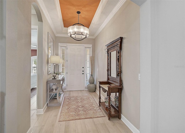 foyer entrance featuring baseboards, light wood-type flooring, a tray ceiling, ornamental molding, and arched walkways