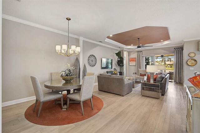 dining area with ornamental molding, ceiling fan with notable chandelier, a tray ceiling, light wood finished floors, and baseboards