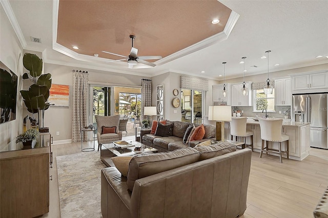 living area featuring visible vents, light wood-style flooring, a raised ceiling, and ceiling fan