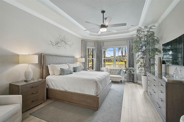 bedroom with ornamental molding, a tray ceiling, a textured ceiling, light wood finished floors, and ceiling fan