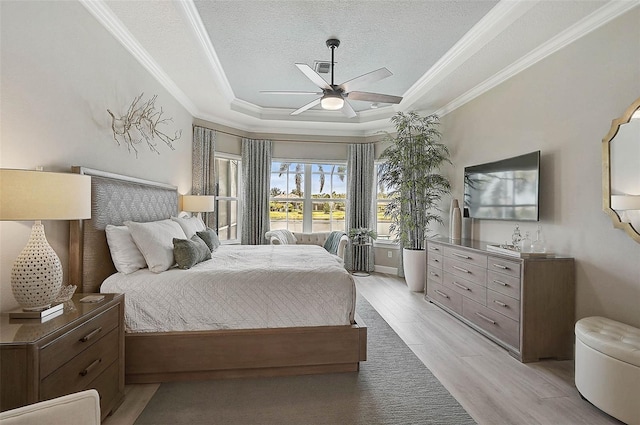 bedroom with a tray ceiling, light wood-style floors, crown molding, and a textured ceiling