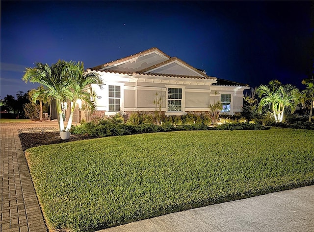 view of front of home featuring a lawn, stone siding, a tiled roof, decorative driveway, and stucco siding