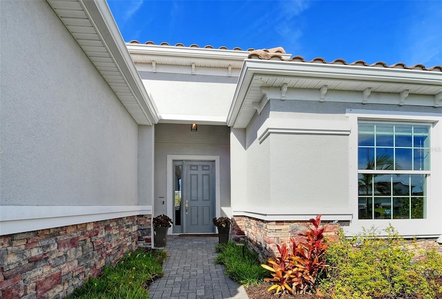 doorway to property with a tiled roof, stone siding, and stucco siding