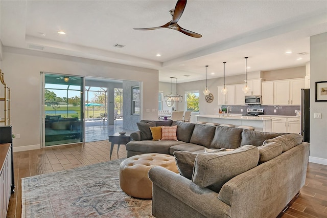 living area with recessed lighting, wood finished floors, visible vents, a ceiling fan, and baseboards