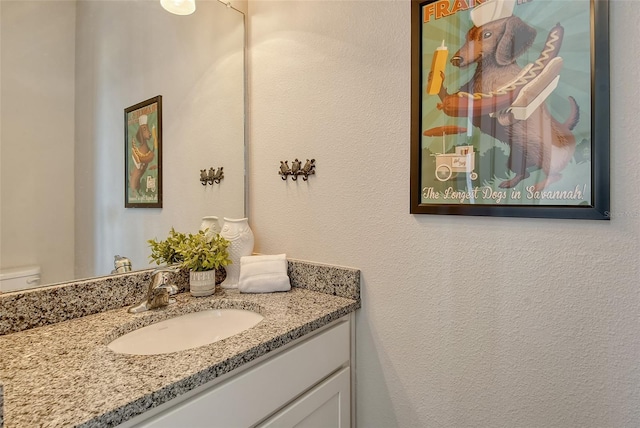 bathroom featuring toilet, a textured wall, and vanity