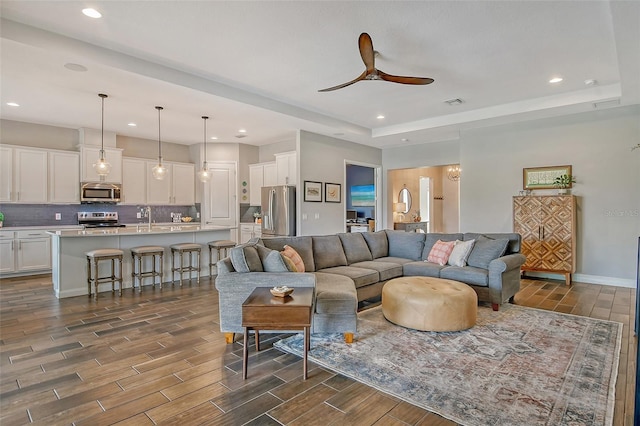 living area with wood tiled floor, a tray ceiling, ceiling fan, and recessed lighting