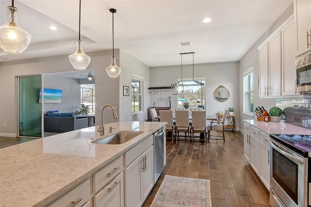 kitchen with dark wood-style floors, light stone counters, stainless steel appliances, white cabinetry, and a sink