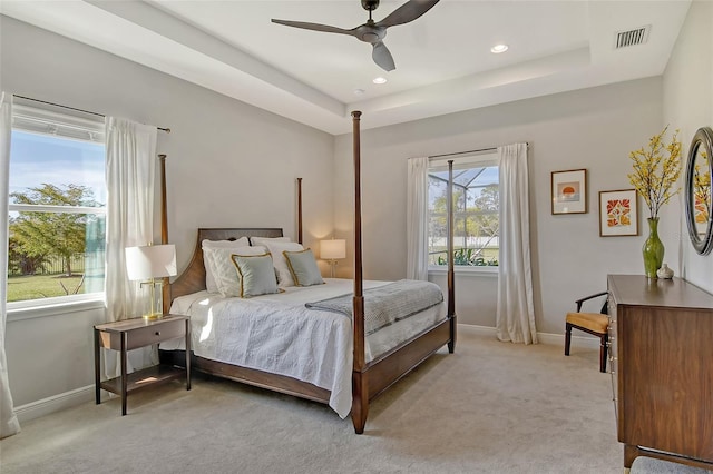 bedroom featuring a tray ceiling, light carpet, visible vents, and baseboards