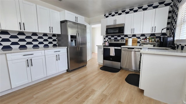 kitchen featuring white cabinets, decorative backsplash, stainless steel appliances, light countertops, and light wood-style floors