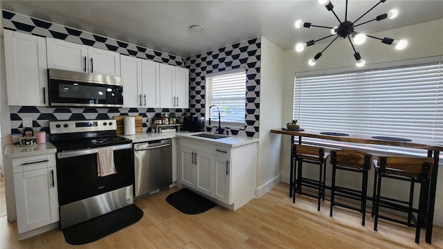 kitchen featuring light wood finished floors, tasteful backsplash, light countertops, appliances with stainless steel finishes, and a sink