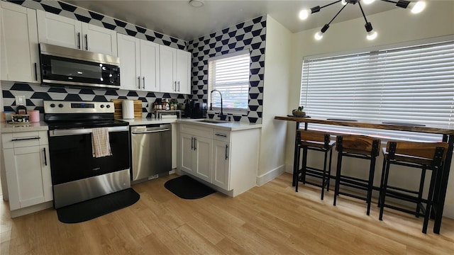 kitchen with stainless steel appliances, a sink, white cabinets, light wood-type flooring, and tasteful backsplash