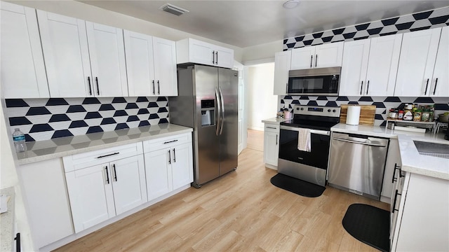 kitchen featuring tasteful backsplash, visible vents, white cabinets, light wood-style flooring, and stainless steel appliances