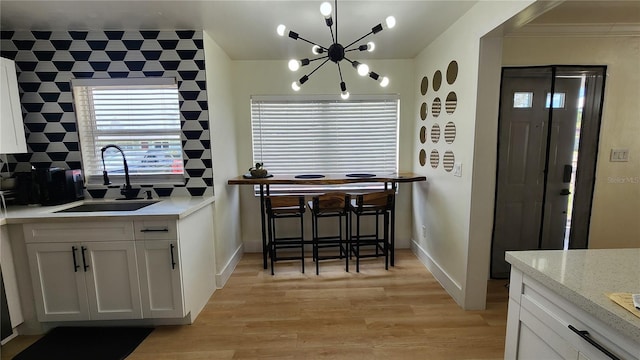 kitchen featuring a notable chandelier, tasteful backsplash, white cabinetry, a sink, and light wood-type flooring