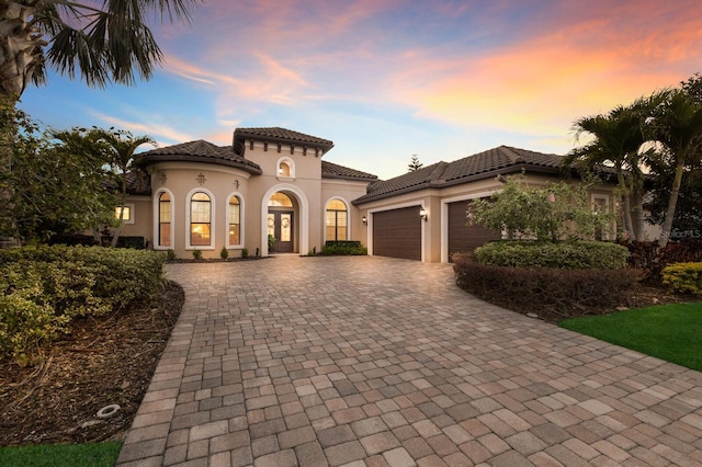 mediterranean / spanish-style house featuring a garage, a tiled roof, decorative driveway, and stucco siding