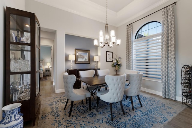 dining space featuring a notable chandelier, wood finished floors, baseboards, ornamental molding, and a raised ceiling