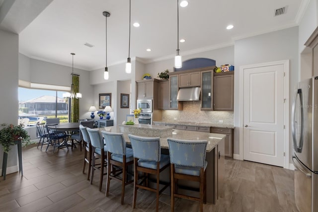 kitchen with under cabinet range hood, stainless steel appliances, wood finished floors, a center island, and tasteful backsplash