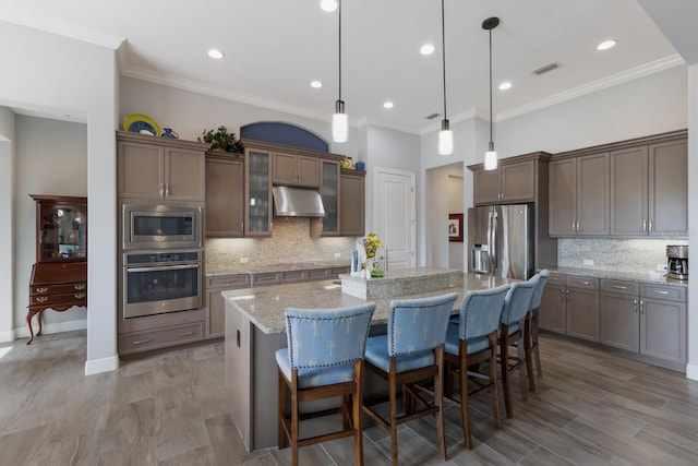 kitchen featuring visible vents, an island with sink, appliances with stainless steel finishes, a breakfast bar area, and under cabinet range hood