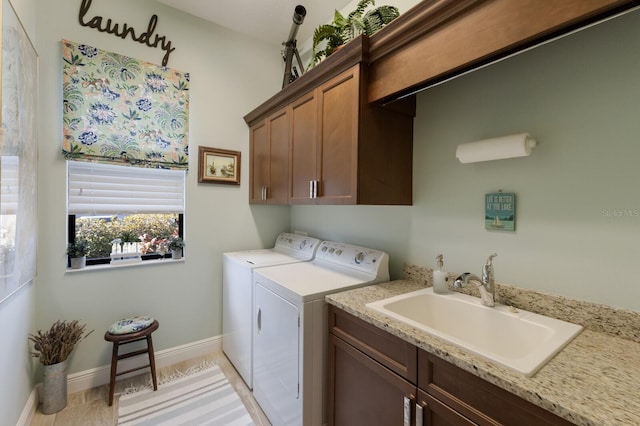 clothes washing area featuring a sink, washing machine and clothes dryer, cabinet space, and baseboards