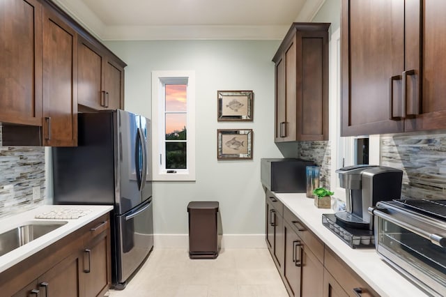 kitchen featuring crown molding, light countertops, backsplash, freestanding refrigerator, and baseboards