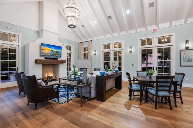 living area with a notable chandelier, visible vents, wood finished floors, high vaulted ceiling, and a warm lit fireplace