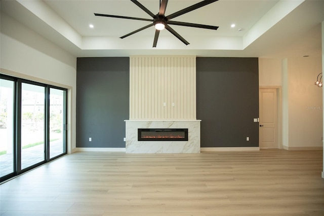 unfurnished living room featuring a fireplace, a raised ceiling, a ceiling fan, light wood-type flooring, and baseboards