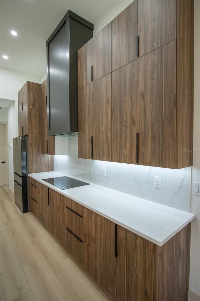 kitchen with tasteful backsplash, light wood finished floors, black appliances, and modern cabinets